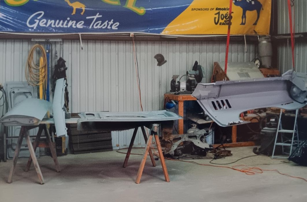 Dan Powell's Oklahoma shop — body panels and fenders stripped and prepped for restoration, laid out on sawhorses under a Camel Racing banner